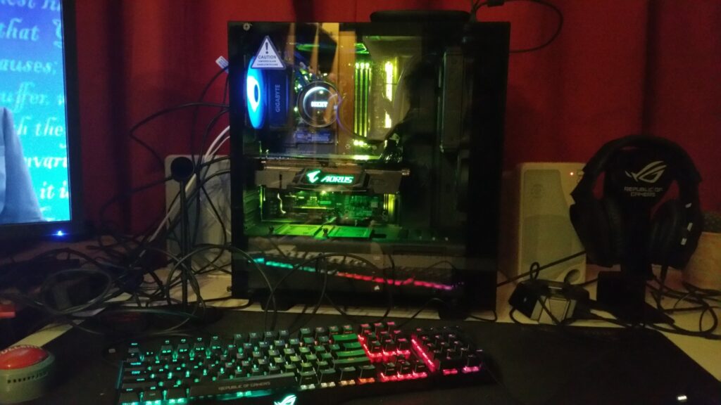 A gaming PC setup with RGB lighting, monitor, keyboard, and headset