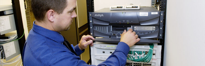 A technician working on a network server rack in a data center, representing the human side of AI infrastructure