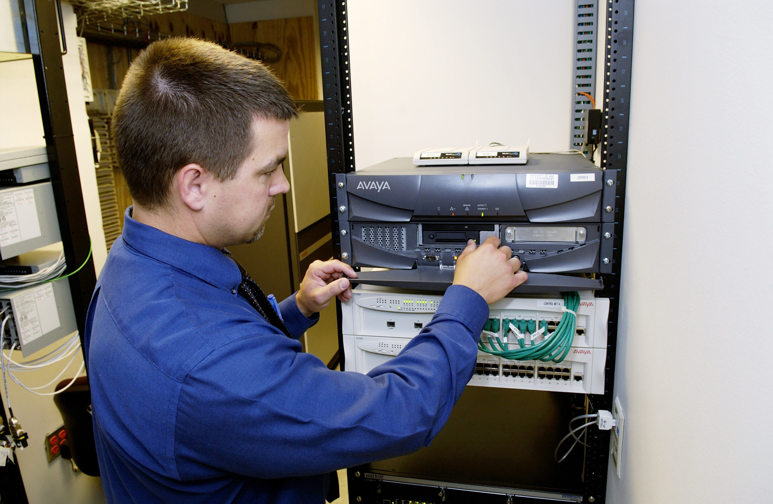 A technician working on a network server rack in a data center, representing the human side of AI infrastructure