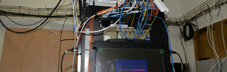 Network server rack with numerous cables and a monitor displaying login credentials on a blue screen representing server administration