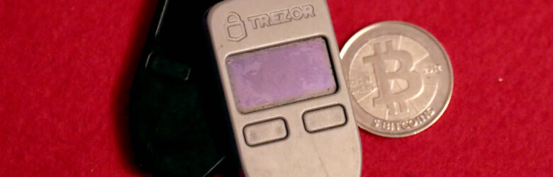 Two Trezor One hardware wallets next to a physical 5 BTC Casascius coin