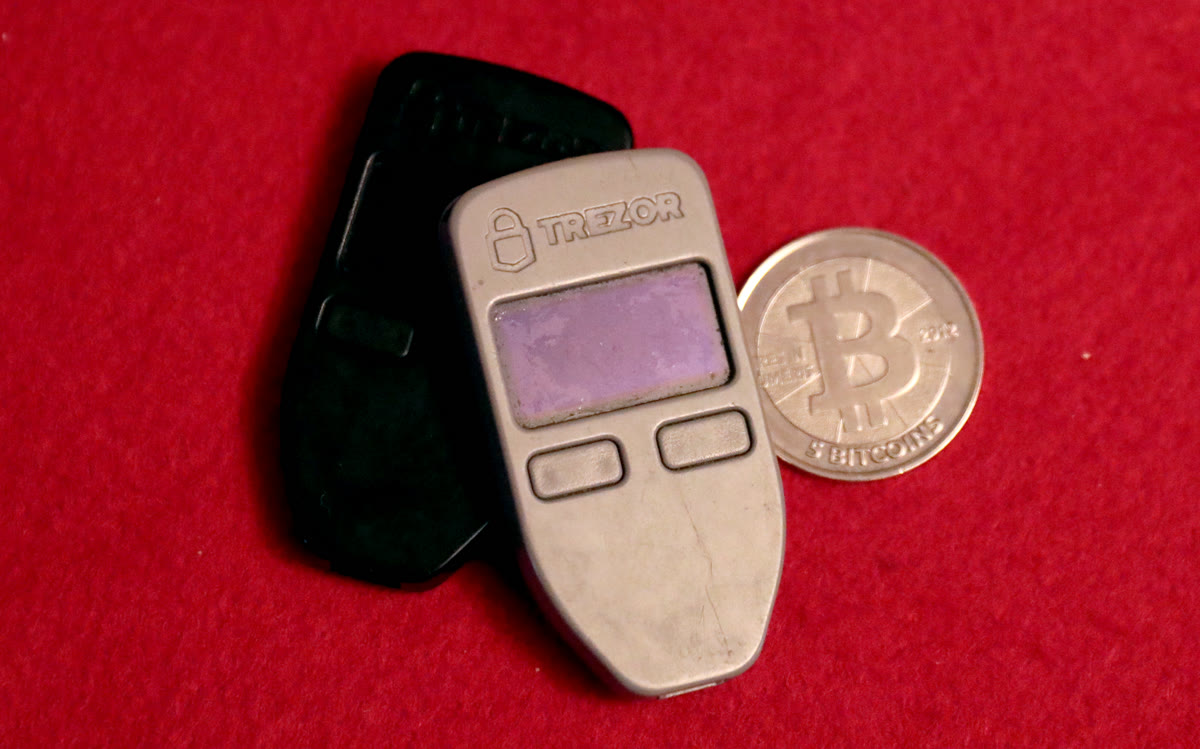 Two Trezor One hardware wallets next to a physical 5 BTC Casascius coin