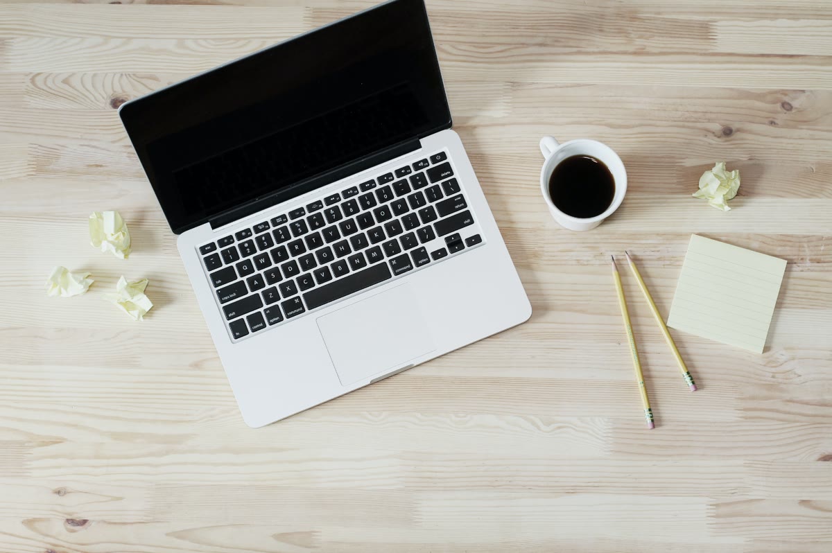 Laptop and a cup of coffee on a wooden desk, representing a developer email footprint audit workspace