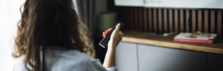 A person sits on a couch watching a smart television while holding a remote control, illustrating smart TV privacy