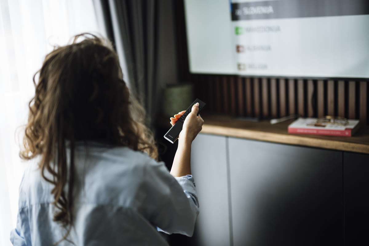 A person sits on a couch watching a smart television while holding a remote control